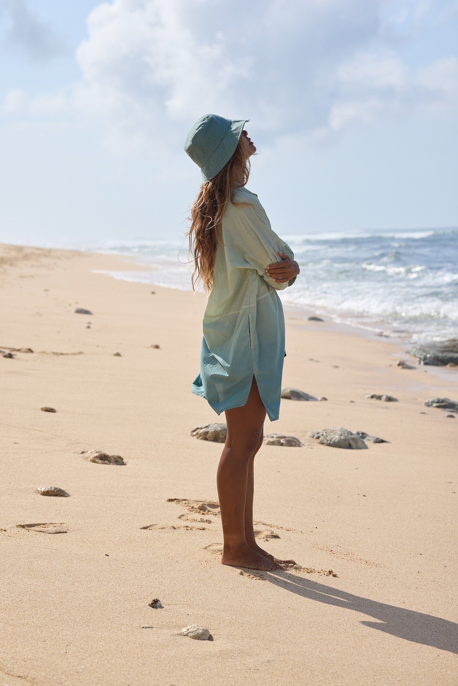 Side view of woman wearing the Tati Shirt Dress made from certified organic cotton, hand-dyed with natural plant pigments in soft aqua tones, designed in New Zealand and crafted slowly in the hills of Bali. Lightweight, sustainable, and perfect for resortwear and everyday summer styling.